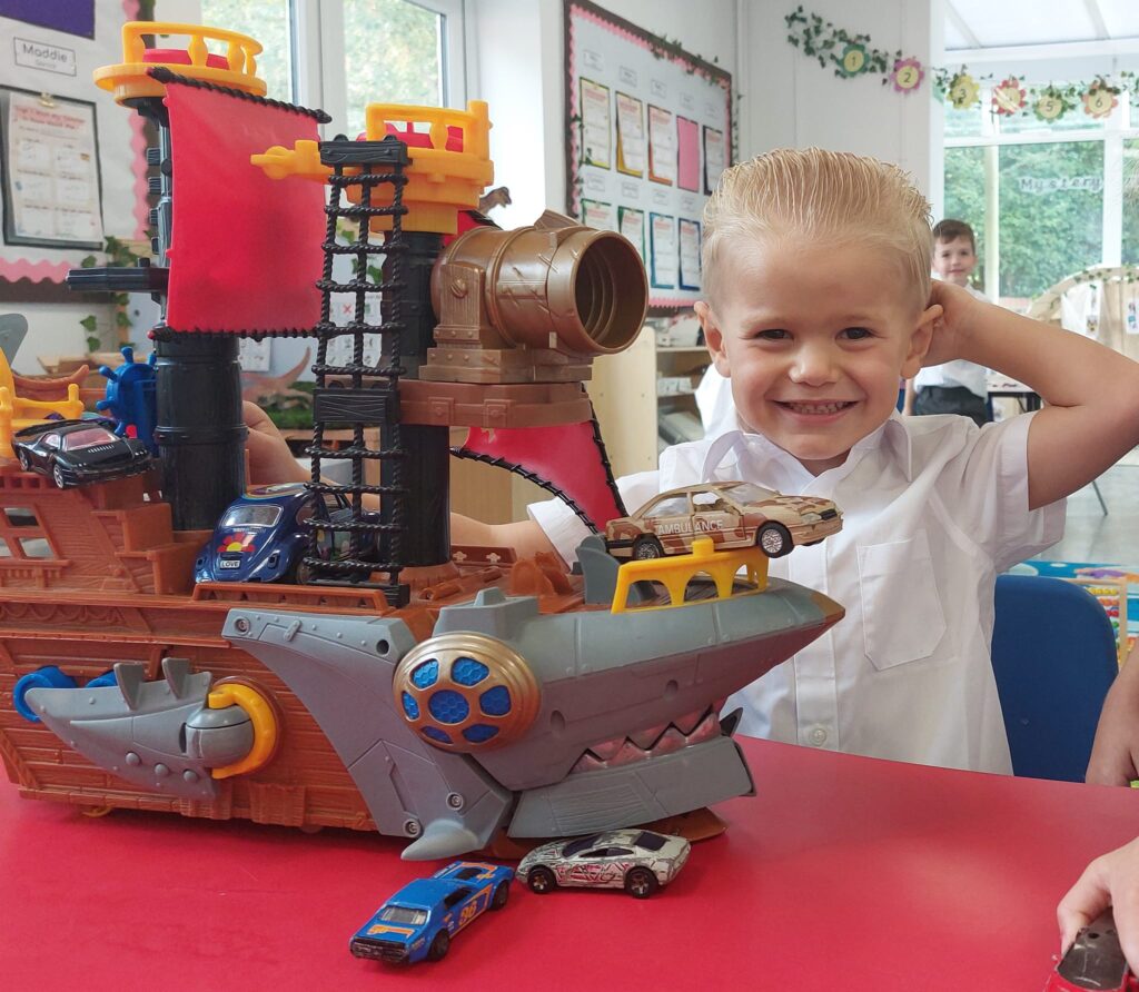 A new EYFS pupil is seen smiling at the camera and playing with some toys.