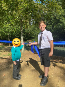 Two Horsmonden pupils, one young and one older, can be seen cutting the ribbon together to open the academy's new outdoor Gym area.