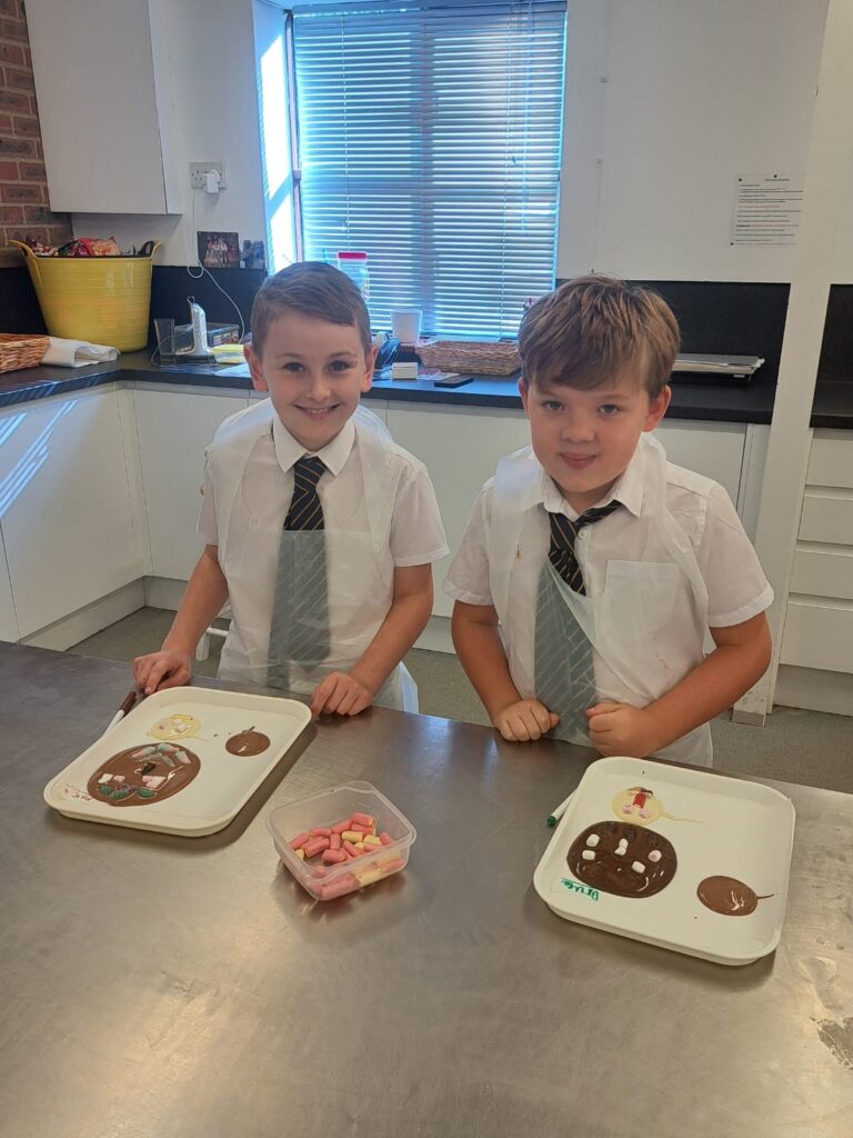 Two Year 4 pupils are pictured smiling for the camera whilst wearing aprons and making chocolate together.