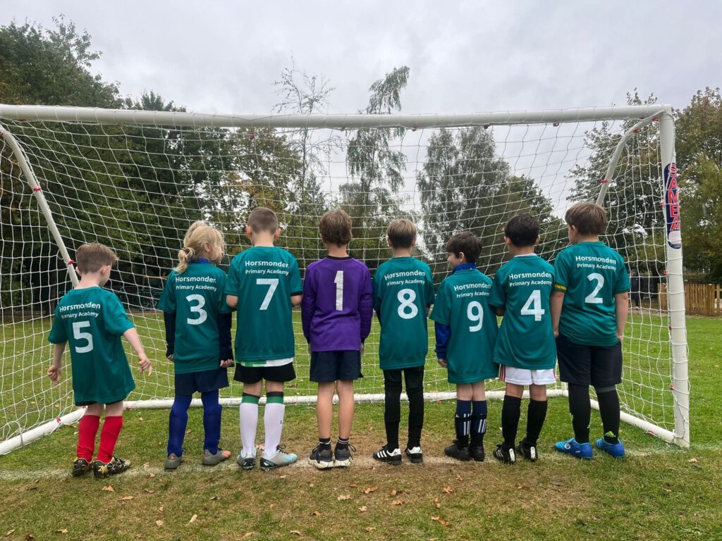 A team of children in football kits smiling for a photo in front of a goal