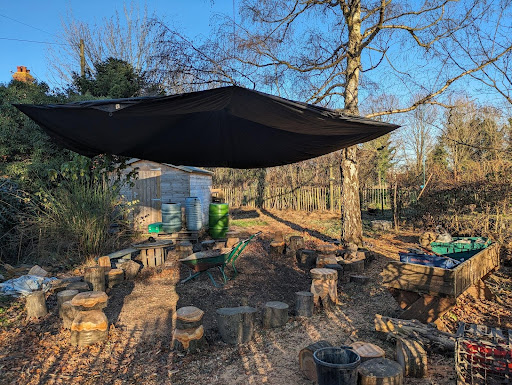 Photo showing the Forest School area on the academy grounds with a canopy set above a group of wooden tree stumps.