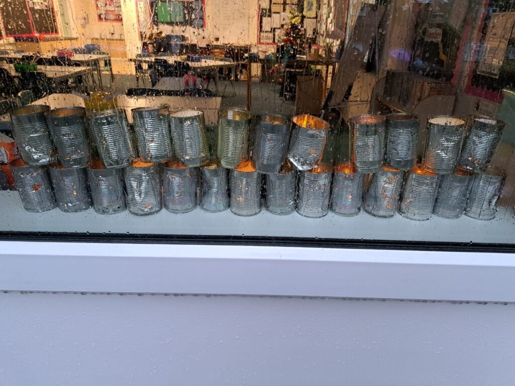 A photo taken from outside, through the window, showing all of the tin can Christmas lanterns created by pupils lit on the window pane.