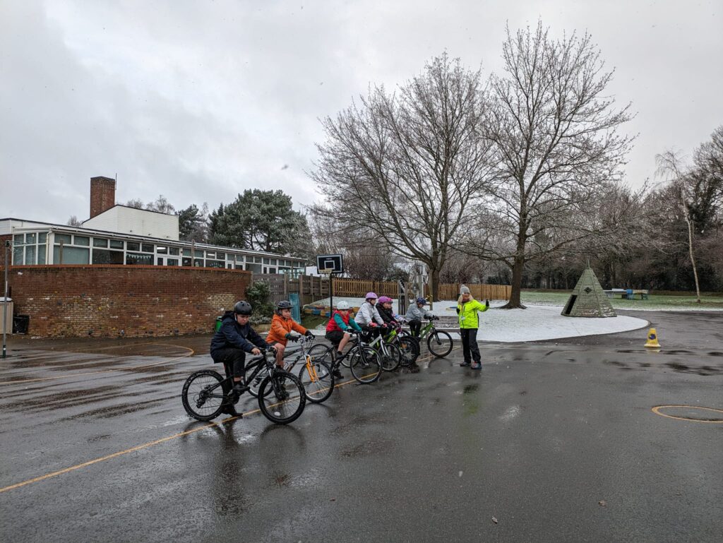 Year 6 pupils participating in Bikeability on the academy playground on a snowy winter's day.