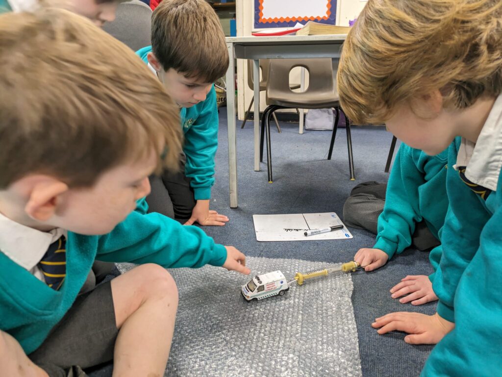 Year 6 pupils are seen experimenting with friction on different materials and surfaces.