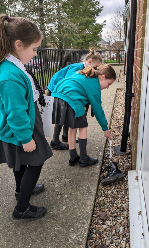 Three girls in Year 6 are seen experimenting with friction by dragging an object across a surface of loose stones on the academy grounds.