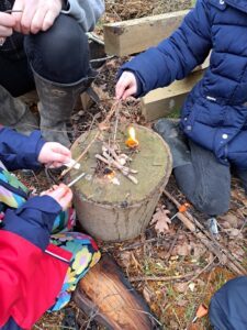 A small group of Year 1 pupils are pictured sat around a campfire in the Forest School on the academy grounds, wearing their winter coats.
