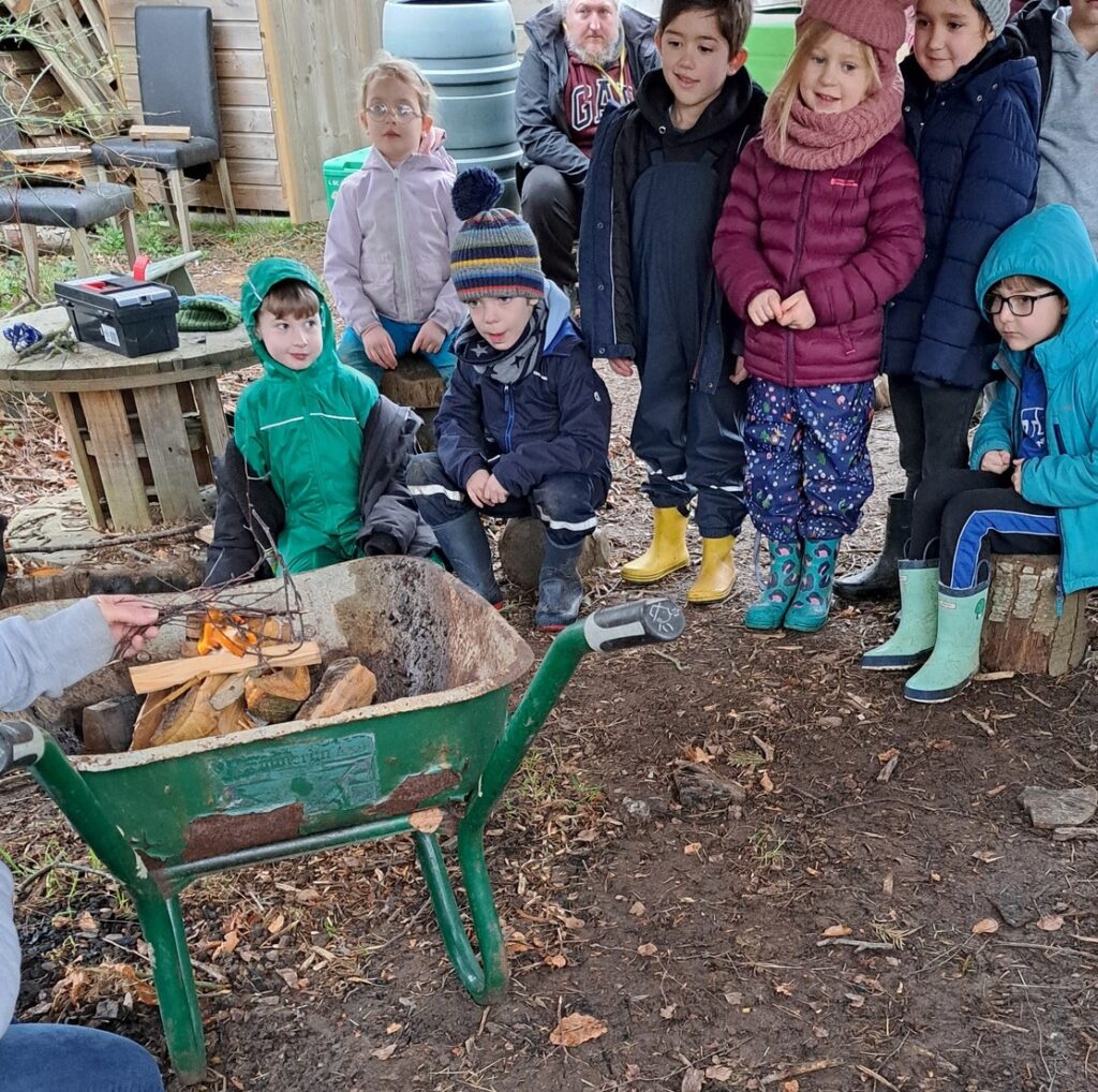 A small group of young pupils are pictured together watching a member of staff demonstrating how to create a campfire in the Forest School.