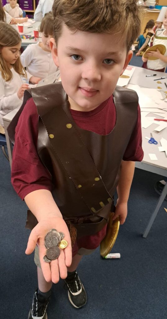 A student smiling for a photo dressed as a Roman, holding coins in his hand